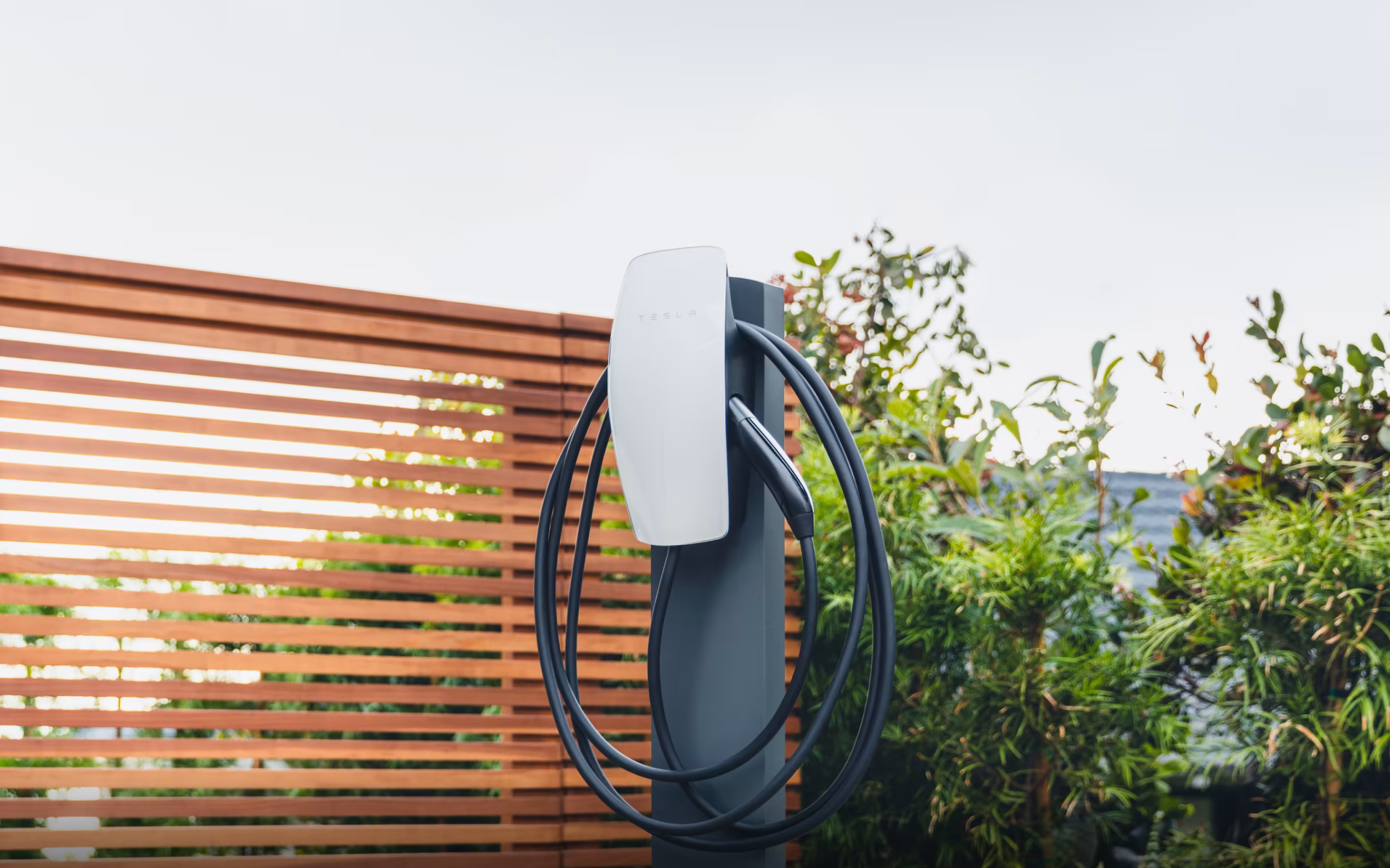 Gen 3 Wall Connector with tempered white glass faceplate mounted on a pedestal in front of a fence